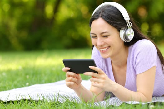 Happy asian woman watching video on phone in a park