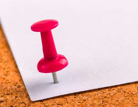 The plastic button with a needle stuck in an iron sheet of white paper on a wooden stopper.