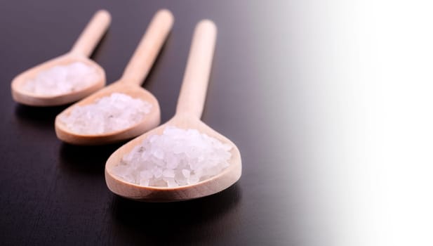 The Bath salt in three wooden spoons on a dark polished desk in backlight