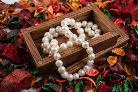 Pearl jewelry in wooden box on dry flowers background.