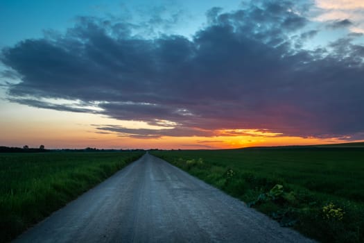 A road through the fields and colorful sunset, spring view