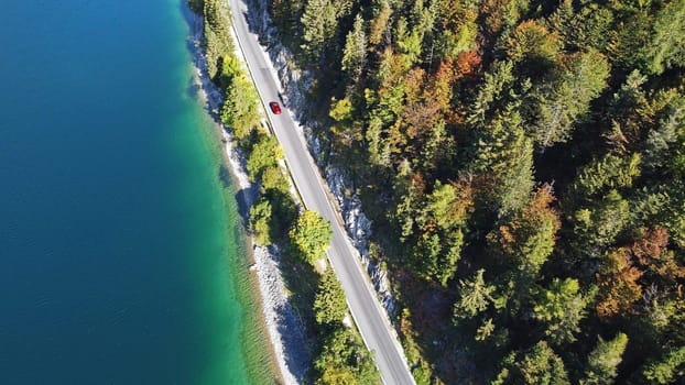 Aerial drone shot of red car road between lake and autumn forest