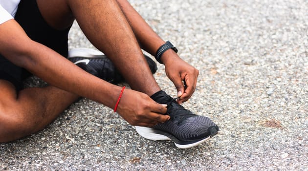 Close up Asian sport runner black man sitting shoelace trying running shoes getting ready for jogging and run at the outdoor street, health exercise workout concept