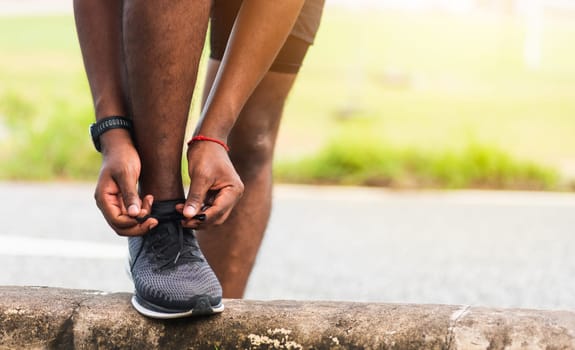 Close up Asian sport runner black man wear watch stand step on the footpath trying shoelace running shoes getting ready for jogging and run outdoor street health park, healthy exercise workout concept
