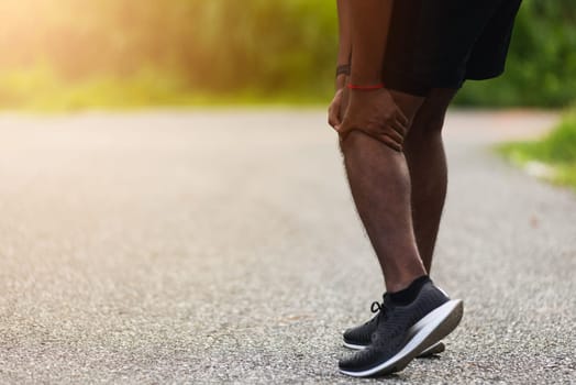 Asian young athlete sport runner black man stand wear feet shoe active running training at outdoor he use hands hold on his knee pain while running, healthy exercise injury osteoarthritis from workout