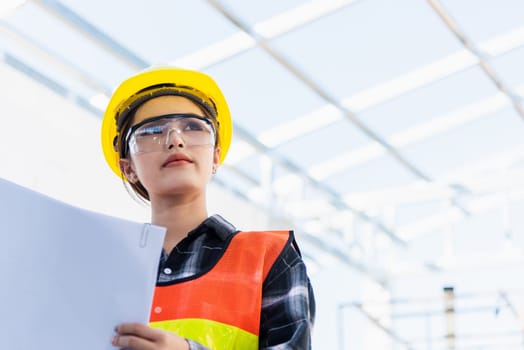 Asian engineer architect worker woman holding blueprint infrastructure progress at construction site, engineering female leader standing hold paper plan control worker to building project