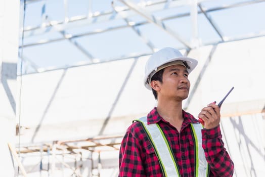 Asian engineer foreman architect worker man working at building construction site talking with radio, engineering hold radio discuss operate and control worker employee to building construction