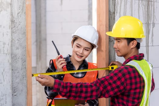 Male industrial builder workers installation process measuring wooden door with measure tape and service woman checking in building construction site. Worker work Building house concept