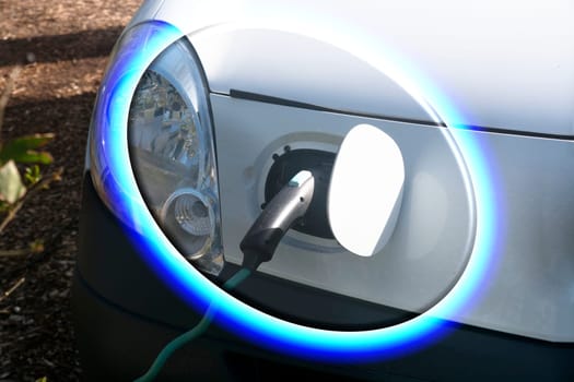 EV car or electric vehicle at the charging station with the power cord adapter plugged into blurred nature with blue energy power effect. Environmentally friendly sustainable energy concept. .