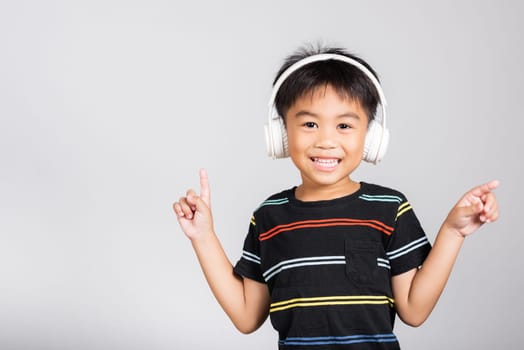 Little cute kid boy 5-6 years old listen music in wireless headphones in studio shot isolated on white background, happy Asian children smiling listening audio and dancing, entertainment lifestyle
