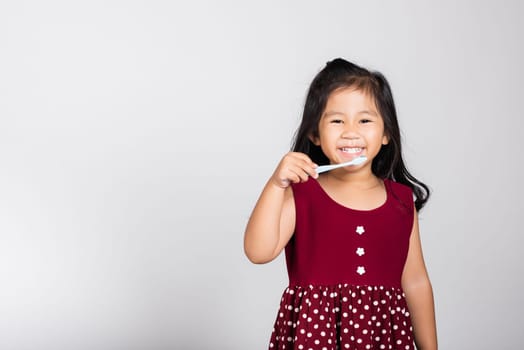 Little cute kid girl 3-4 years old brushing teeth and smile in studio shot isolated on white background, happy Asian children holding toothbrush in mouth by himself, Dental hygiene healthy concept