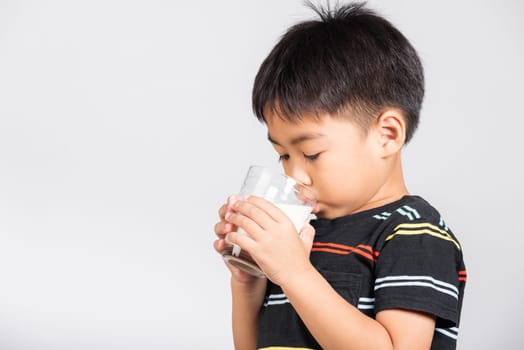 Little cute kid boy 5-6 years old smile holding milk glass he drinking white milk in studio shot isolated on white background, Asian children preschool, Daily life health care Medicine food