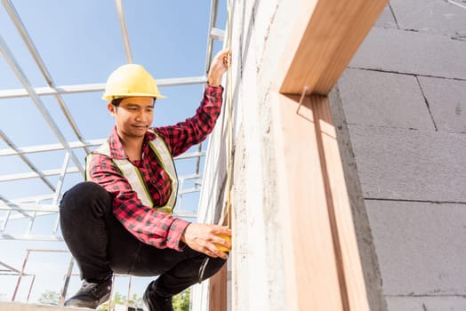 Construction worker or contractor man using measuring tape checking from steel  roof frame to the door on building construction site, foreman taking measurements wall while working