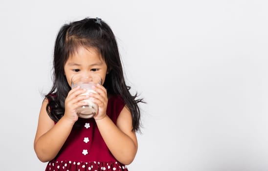 Little cute kid girl 3-4 years old smile holding milk glass he drinking white milk in studio shot isolated on white background, Asian children preschool, Daily life health care Medicine food