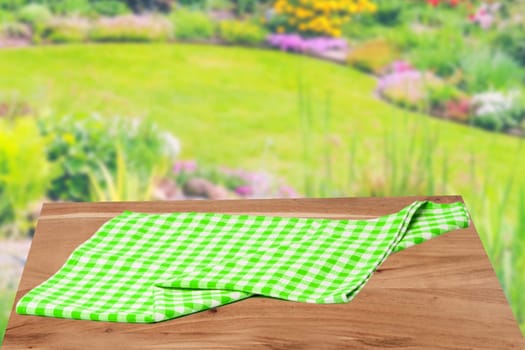 Empty table product. Empty wooden deck table covered with a green white checkered tablecloth over abstract blurred natural backdrop. Space for your food and product display montage.