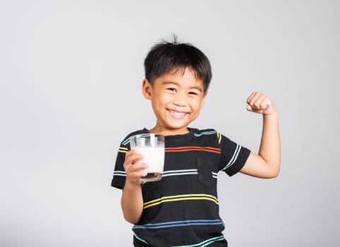 Little cute kid boy 5-6 years old smile holding milk glass and show power strong gesture in studio shot isolated on white background, Asian children preschool, Daily life health care Medicine food