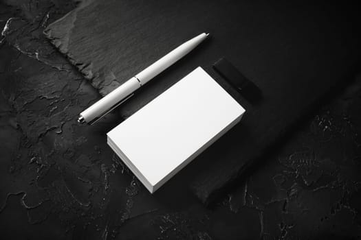 Photo of blank business cards, pen, usb flash drive and slate plate on black stone background. Branding mock up.