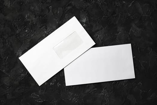 Blank white paper envelopes on black stone background. Front and back side. Template for your design. Flat lay.