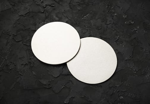 Photo of two blank beer coasters on black stone background.