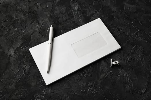 Photo of blank paper envelope, pen and clip on black stone background. Blank stationery template.