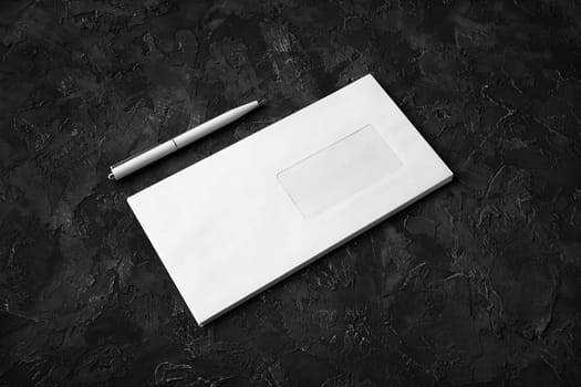 Blank envelope and pen on black stone background.