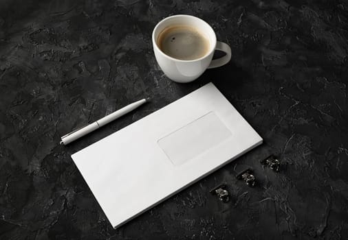 Photo of blank envelope, coffee cup, pen and clips on black stone background. Branding mock up.