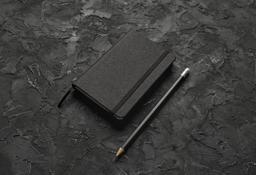 Blank black notebook and pencil on black stone background.