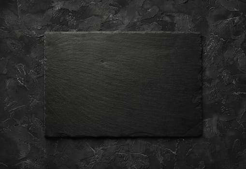 Black stone slate plate on black stone background. Copy space for text. Flat lay.