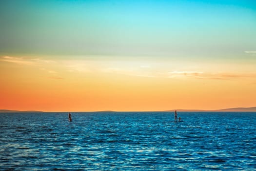 Sunset, blue sea and four people on a two sup boards on the seas. A beautiful sunset with blue and orange colors of the sky..
