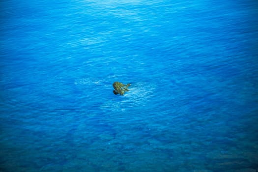 The stone peeks out of the sea. The blue sea surrounds the top of the stone.