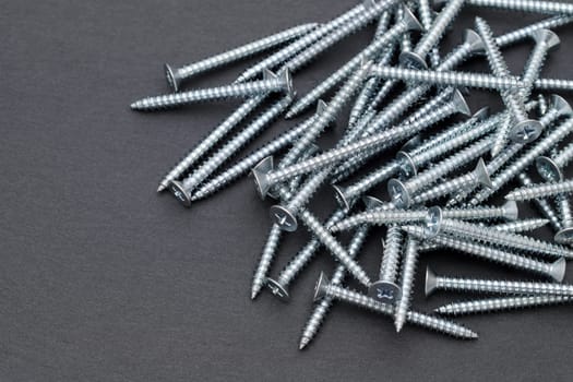 Pile of silver metallic tapping screws on black background