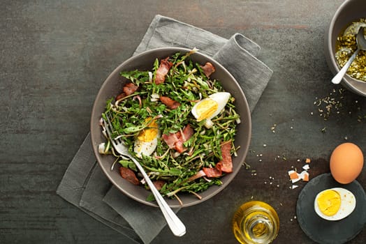 Fresh dandelion salad with bacon and eggs on grey background