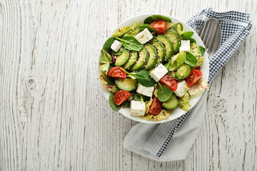 Healthy green salad with avocado and feta cheese on wooden table
