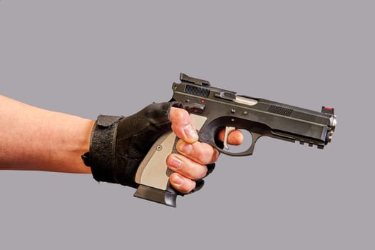 A man's hand holds a black pistol in his hand on a gray background. High quality photo