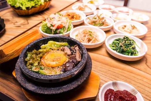 Bibimbap in a black heated stone bowl, Korean traditional dish- bibimbap mixed rice with vegetables Include beef and fried egg and pickles set on table, Japanese hot pot food