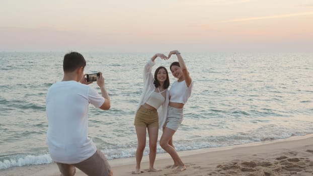 Happy friends smiling and posing taking photo from smartphone and having fun together on beach in holiday vacation time at sunset, Young Asian group woman and man in summer travel outdoor