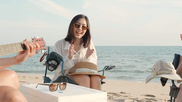 Happy friend have fun playing guitar and clap in camp they smiling together in holiday on sand beach near camping tent vacation time at sunset, Young Asian group woman and man in summer travel outdoor