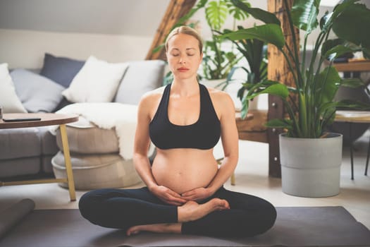Young beautiful pregnant woman training yoga, caressing her belly. Young happy expectant relaxing, thinking about her baby and enjoying her future life. Motherhood, pregnancy, yoga concept