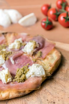 Italian pizza on wooden cutting board. In the blurred background, cherry tomatoes and mozzarella.