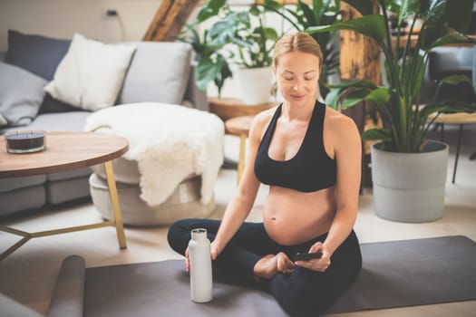 Young happy and cheerful beautiful pregnant woman chating to family and friends on mobile phone while staying fit, sporty and active on her maternity leave. Motherhood, pregnancy, yoga concept