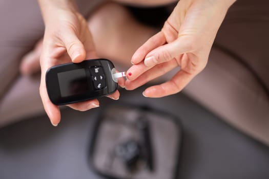 Blood sugar testing at home. Woman checking blood sugar level by glucometer and test stripe at home. Diabetic checking blood sugar levels