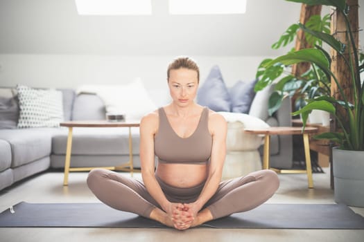 Young beautiful pregnant woman practising yoga at home in her living room. Motherhood, pregnancy, healthy lifestyle, well being and yoga concept