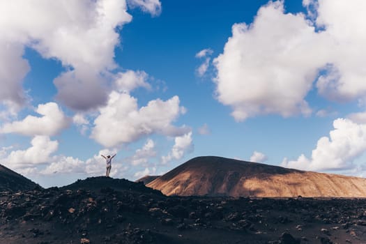 Woman rising hands up in the sky, enjoying amazing views of volcanic landscape in Timanfaya national park on Lanzarote, Spain. Freedom and travel adventure concept
