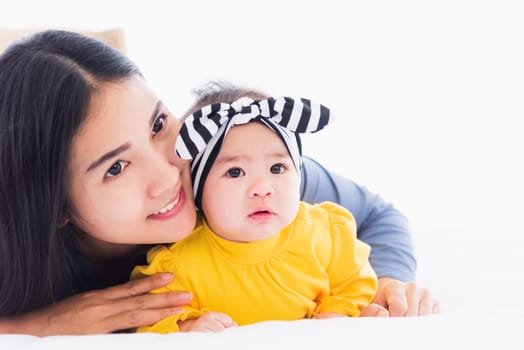 Portrait of beautiful young Asian mother playing and smiling together with his newborn little baby at home, Parent mom and little kid relaxing in the bedroom, Family having fun together