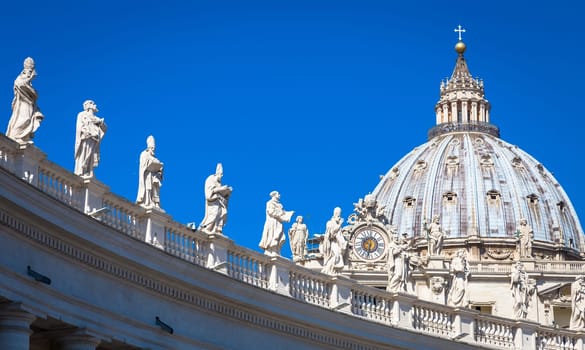 Statues of Catholic Saints. Decorations on Bernini colonnade, Saint Peter Cathedral, with the Cupola in background - Rome, Italy