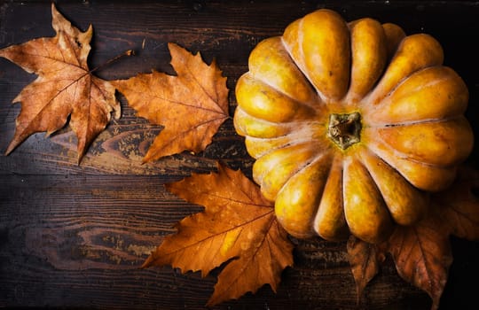 Autumn holiday concept. Pumpkin and maple leaves on rustic wooden table.