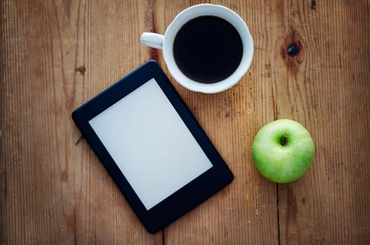 E-book reader, green apple and coffee cup on wooden table