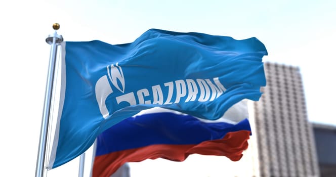 Moscow, RUS, February 2022: Flag with the Gazprom logo waving in the wind with the flag of Russia in the background. Gazprom is a Russian majority state-owned multinational energy corporation