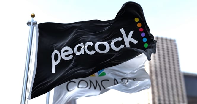 New York, USA, January 2022: Flag of Peacock TV waving in the wind with the Comcast flag in the background. Peacock is an American video streaming service owned by NBCUniversal