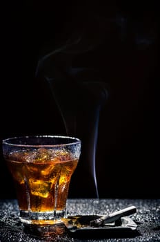 Glass of cold alcohol drink and cigarette over black background